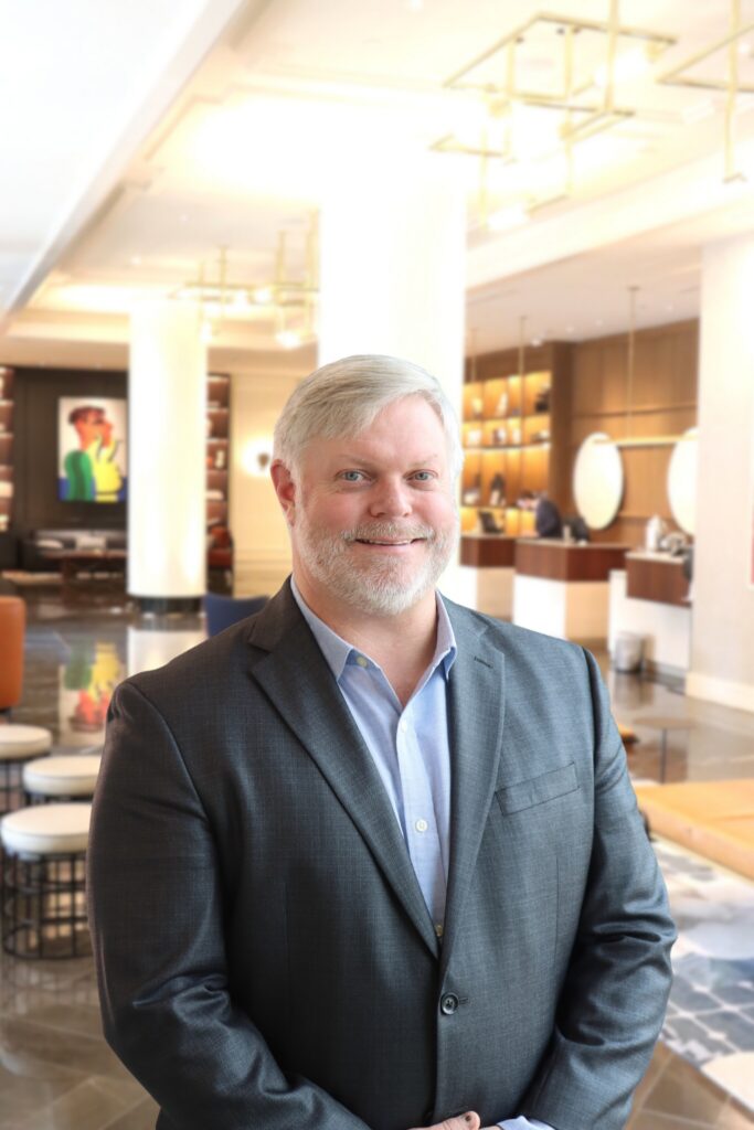 Seth Bush smiling in a suit in a modern lobby setting