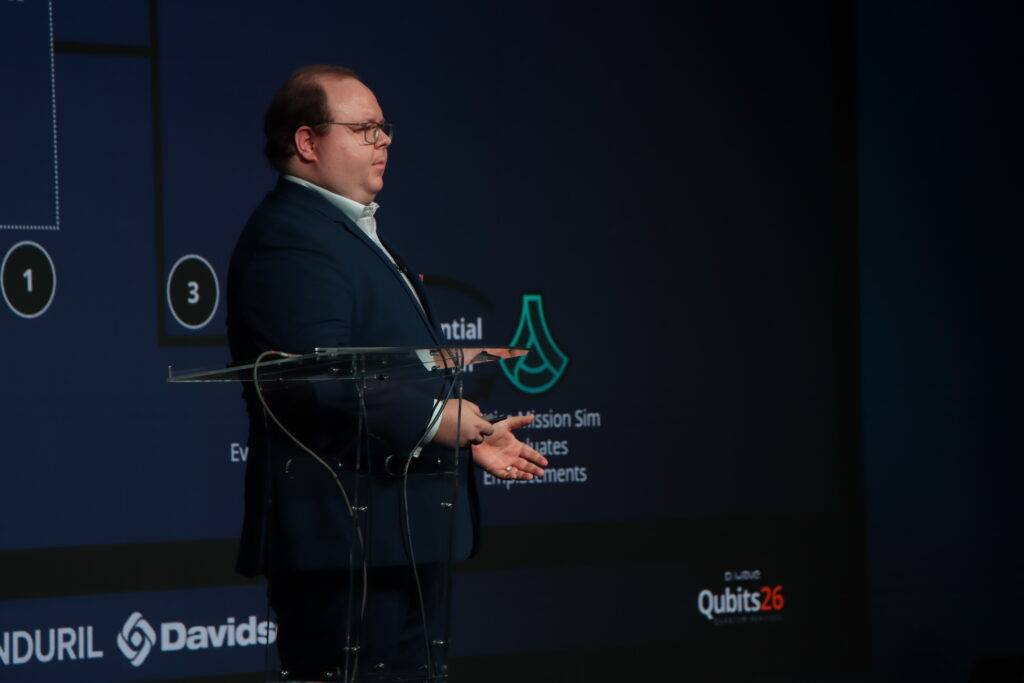 Man speaking at a podium during a conference presentation with a slide displayed behind him